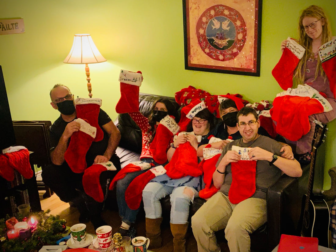 A group of people sit on a couch and smile at the camera. They each hold several red and white Christmas stockings.